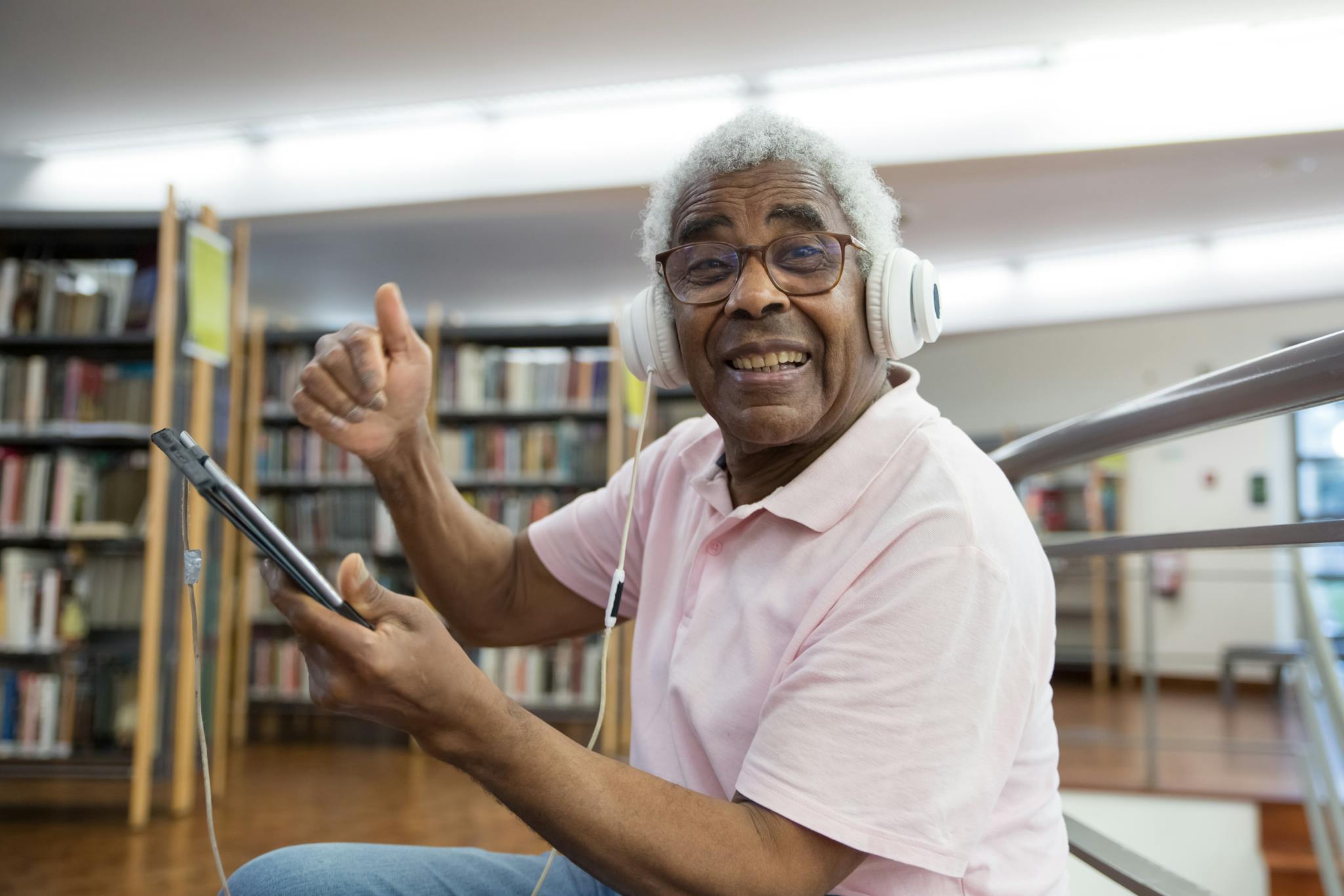 About Us Elderly Man In A Library Smiling With Headphones And Tablet Embracing Digital Learning. 7983604 2048x1365