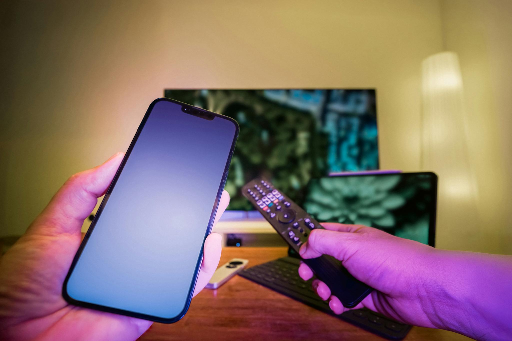 About Us Hands Holding A Smartphone And Remote Control In A High Tech Home Setup With Tv And Other Electronic Devices. 31121857 2048x1366